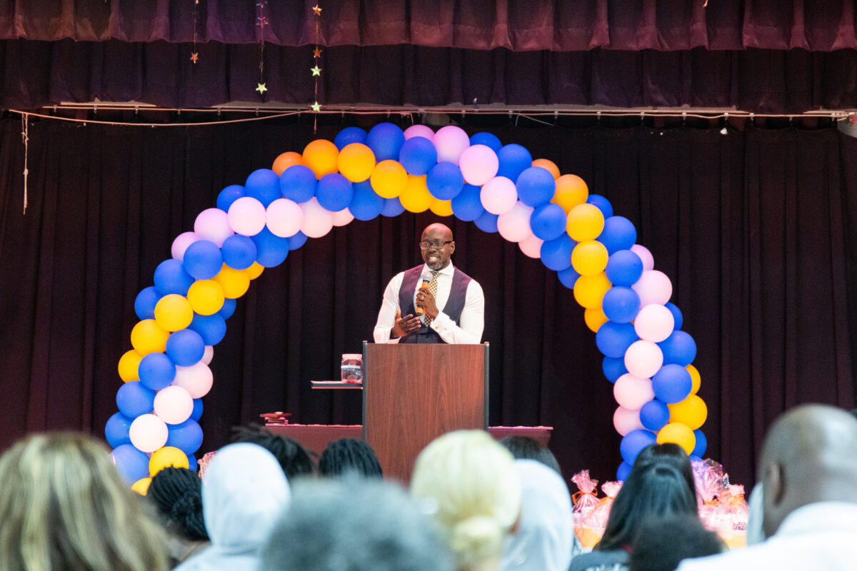 Man speaks at podium on stage at event.