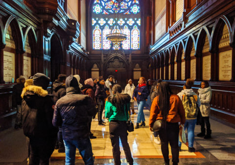 Center for Higher Education and Career Support scholars on a college visit trip gather in a hall as a university representative shares information about the school