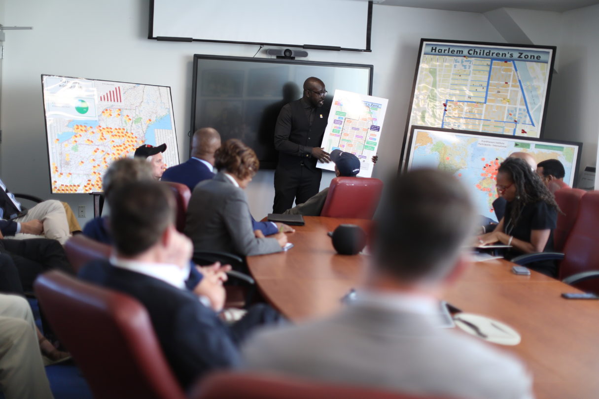replicate our success | HCZ CEO explains a map to people sitting around a board table and taking notes.
