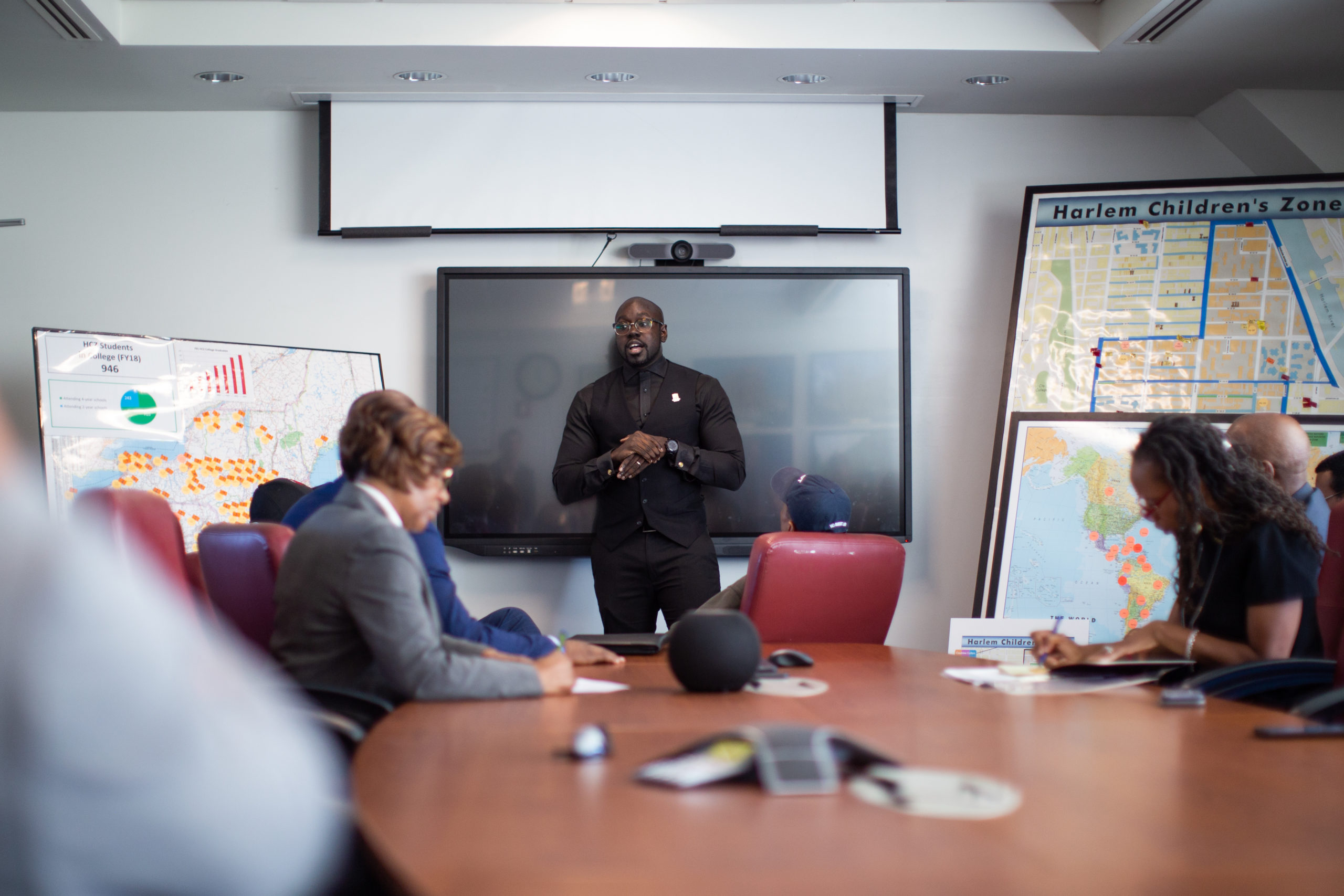 A man is speaking in the front of a room during a meeting