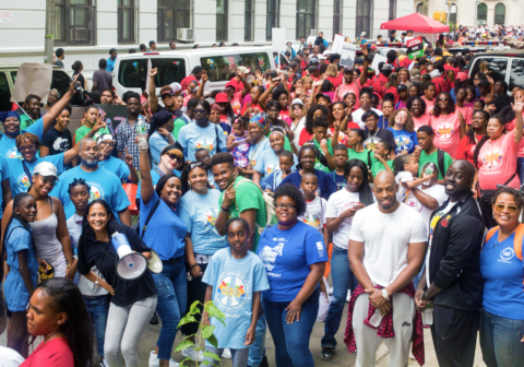 A large group of people who have gathered for a photo after completing a walk for a cause, smile, and celebrate.