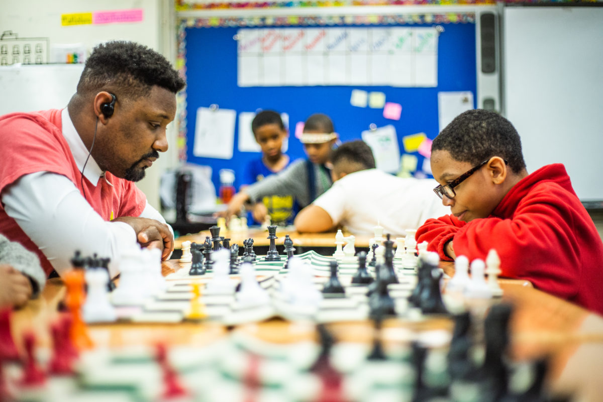 A teacher and student sit at a table playing chess