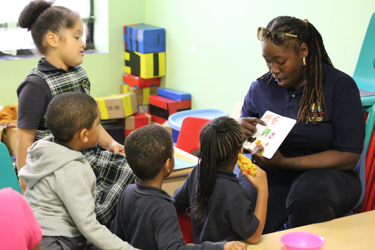 A teacher reads a book and points to animals on the page as preschool students listen and look on