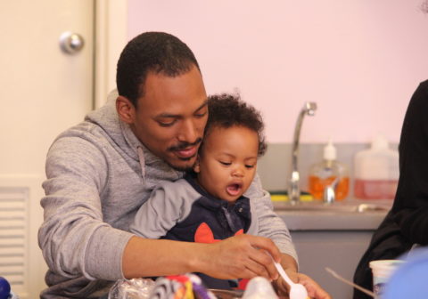Fathers | With his toddler son sitting on his lap, a father and son do arts and crafts in a classroom