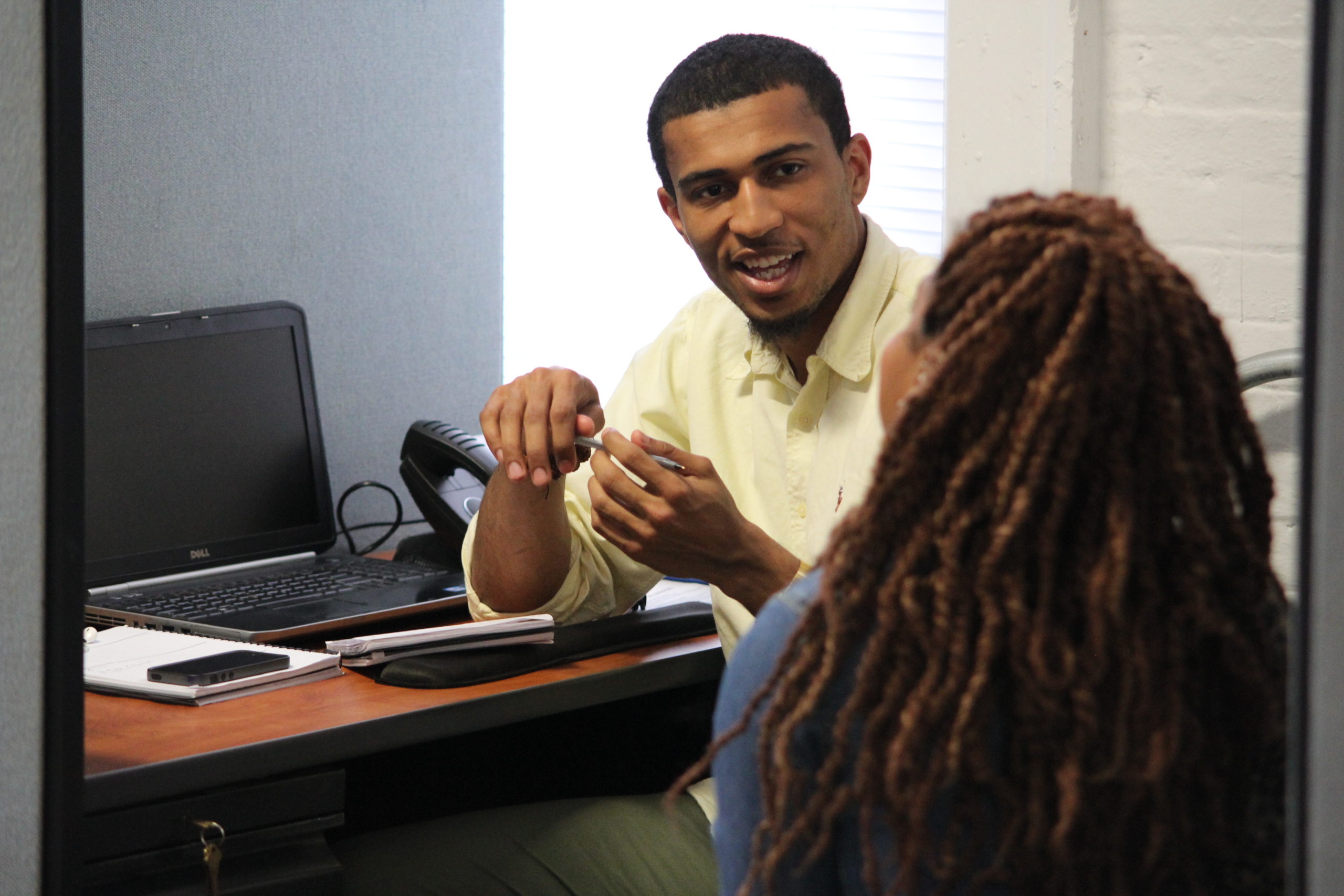 A man and a woman speak to each other at a desk.