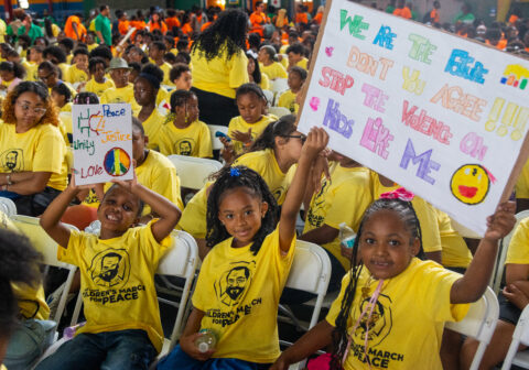 Children in yellow t-shirts smile and wave.