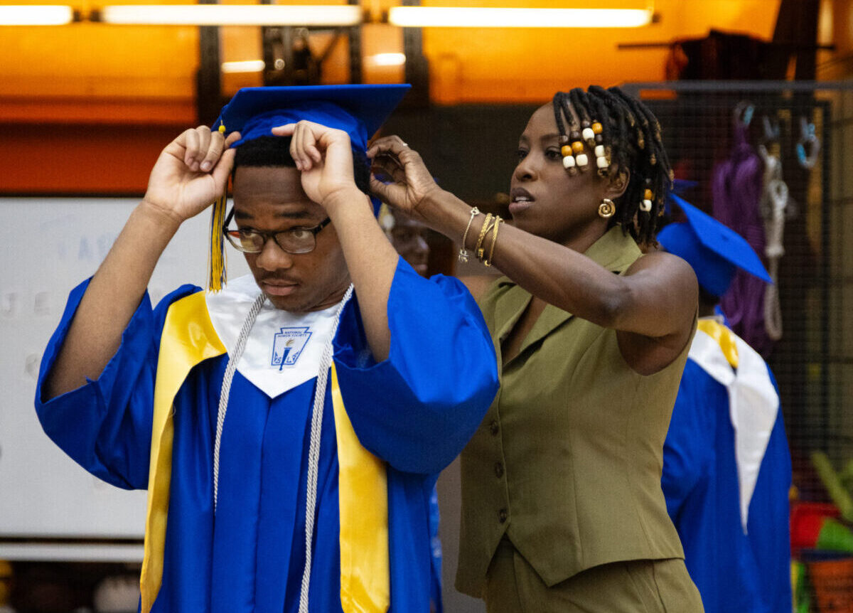Staff assist graduating scholar with his cap.