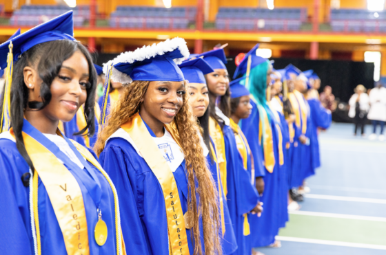Teenagers in blue graduation uniforms standing in gynasium.