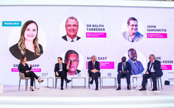 Five people sit on a large stage talking with white background at Alef Education Summit in Dubai, United Arab Emirates.