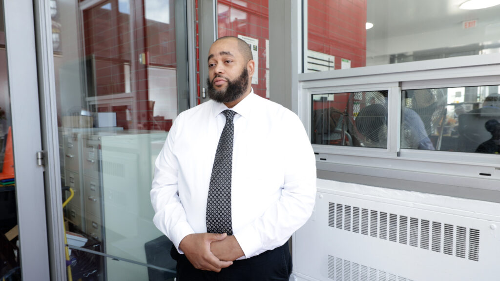 Randy Archer wears a white button down shirt with a tie and stands in the lobby of Promise Academy II.