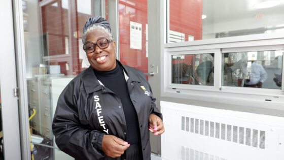 Jasmine Tumma, wearing a jacket with the text "Safety" on it, smiles and stands in the lobby of Promise Academy II.
