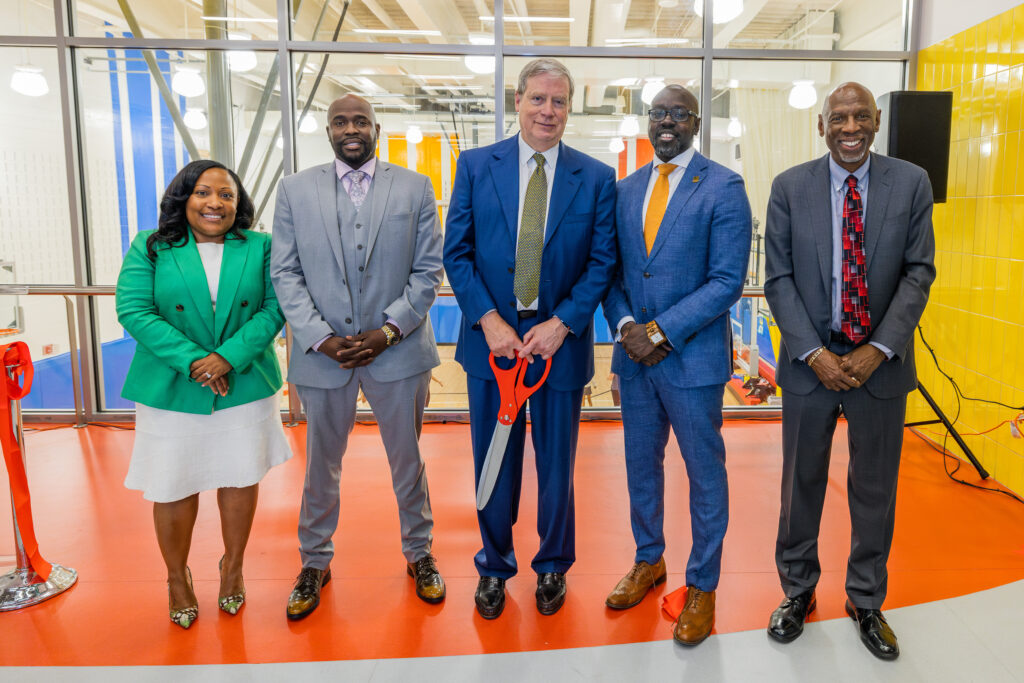 Saskia Brown, Achil Petit, Stanley F. Druckenmiller, Kwame Owusu-Kesse, and Geoffrey Canada stand at the ribbon-cutting ceremony. Stanley holds a large pair of scissors.