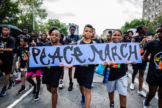 A group of students walk down the street carrying a sign that reads "Peace March."