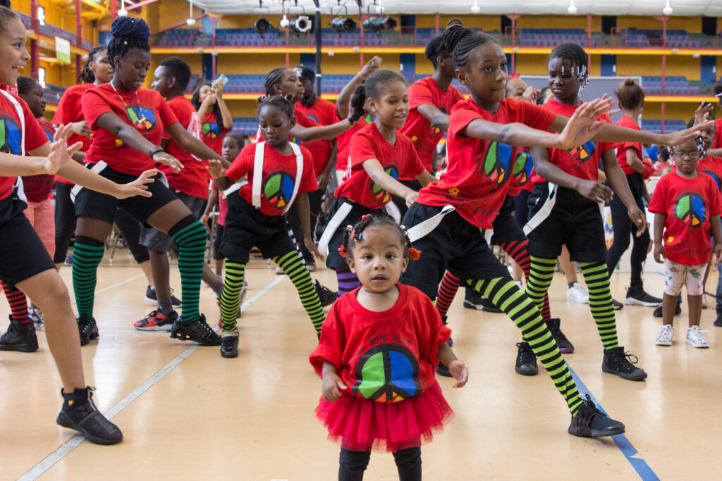 A group of students, wearing matching red T-shirts and striped green tights, perform a dance.