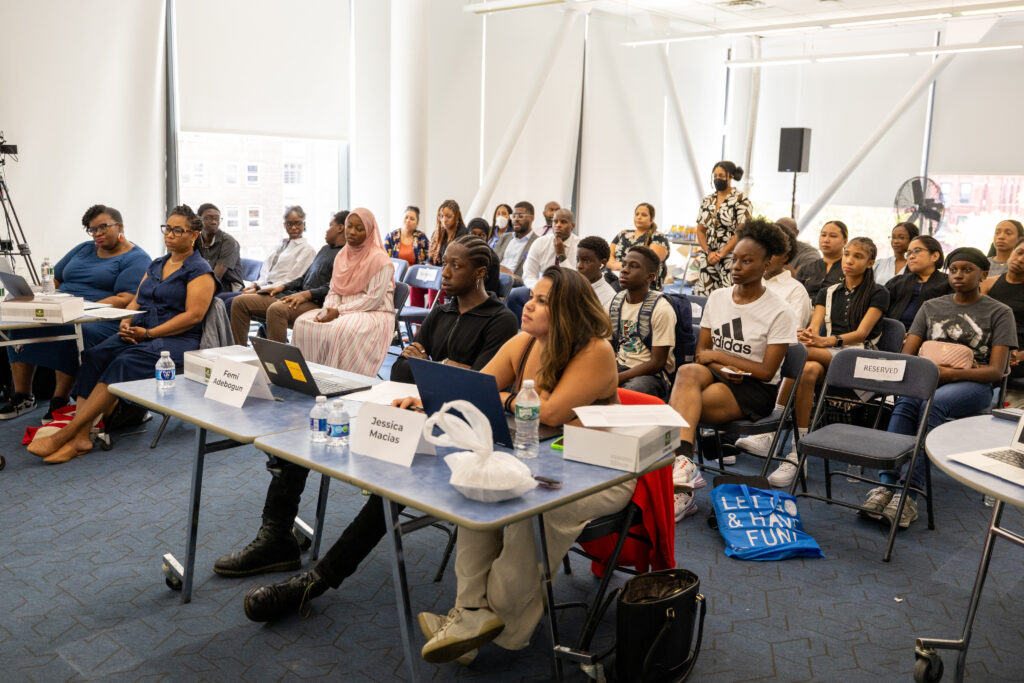 Students and staff members sit behind a panel of judges.