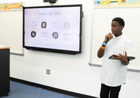 A student stands in front of a whiteboard, delivering a presentation.