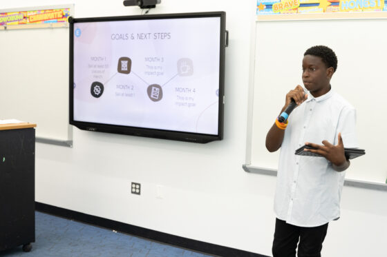 A student stands in front of a whiteboard, delivering a presentation.