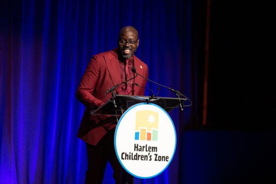 Kwame Owusu-Kesse, wearing a red suit, stands at a lectern.