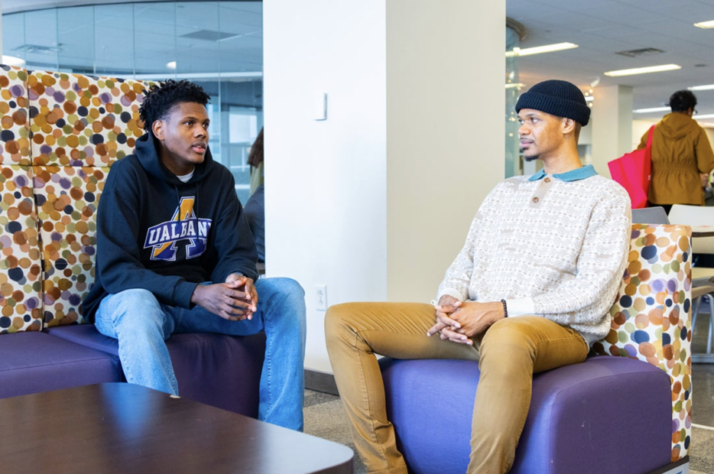 Brandon Sydnor conversing with Hakeem on couches.