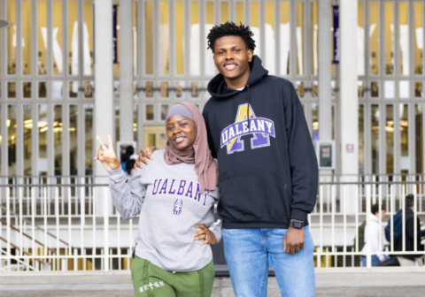 Two students. Brandon Sydnor, a male student in a black sweatshirt with the text "U-Albany" on it, and a female student wearing a headscarf and a gray sweatshirt with purple "U-Albany" lettering on it.