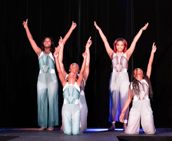 A group of students in dance costumes pose at the end of a dance routine.