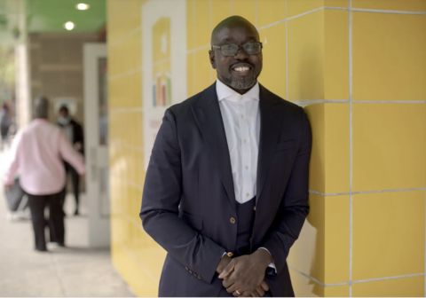 Kwame Owusu-Kesse stands outside of a Harlem Children's Zone building in a suit.
