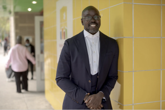 Kwame Owusu-Kesse stands outside of a Harlem Children's Zone building in a suit.