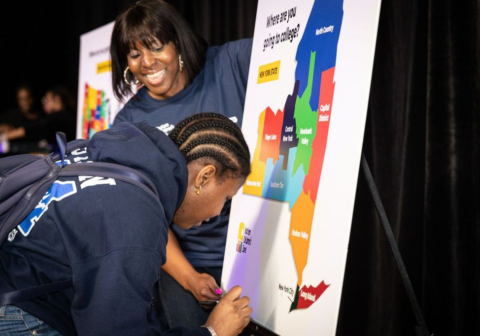 A student in a sweatshirt adds pin to national map to indicate where she will go to college.