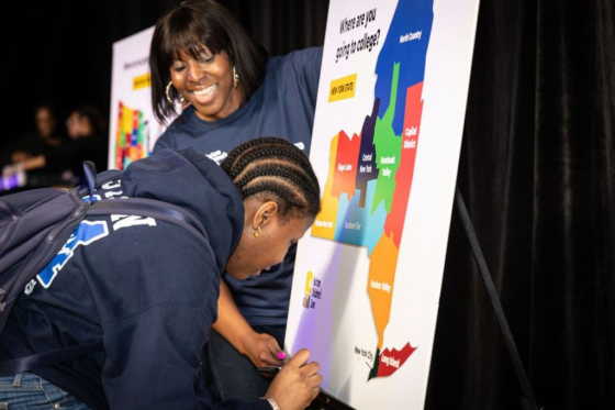 A student in a sweatshirt adds pin to national map to indicate where she will go to college.