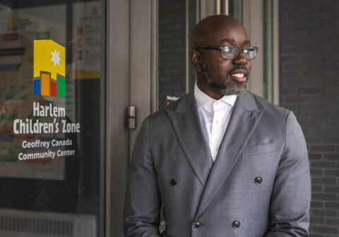 Kwame Owusu-Kesse stands outside a door emblazoned with the Harlem Children's Zone logo.