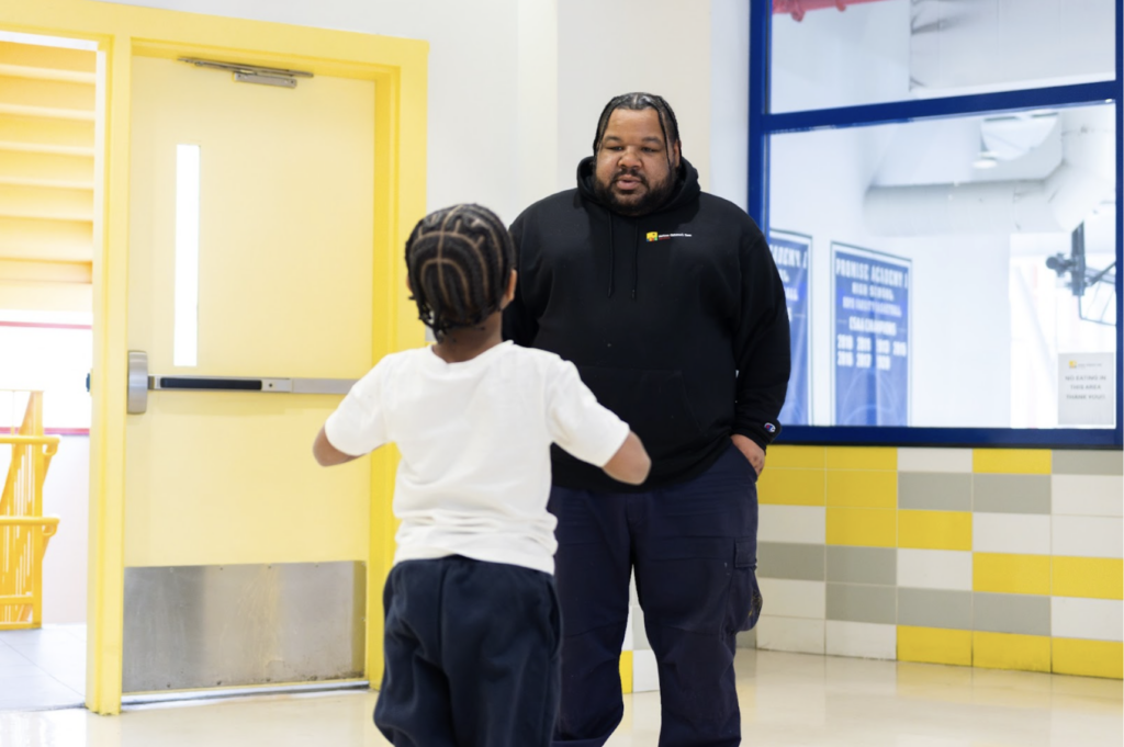 Facilities team staff member stands in the school lobby speaking to a student.