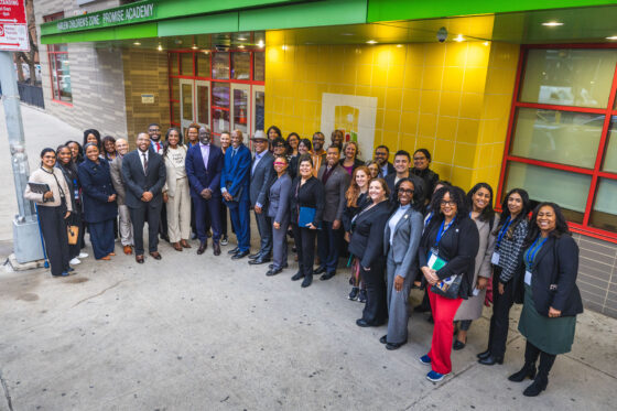 A group of mayors stands in front of a yellow wall outside the school building