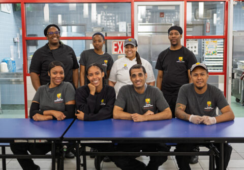 Eight food services professionals pose for a group picture in the cafeteria.